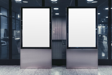 A template of two empty white vertical banners indoors; a mock-up of two blank billboards in the interior of a shopping mall or an airport terminal waiting hall in front of the glass wall; neon light