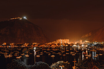 Fototapeta na wymiar A night long-exposure shot of a bay of Botafogo district of Rio de Janeiro, Brazil, with plenty of sailboats, slightly swaying on the water, a mountain peak Sugar Loaf, and residential houses behind