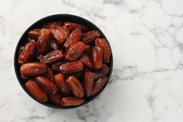 Sweet dried dates in bowl on white marble table, top view. Space for text