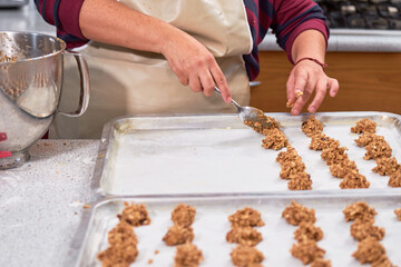 Woman places unbaked oatmeal cookies on steel tray.
