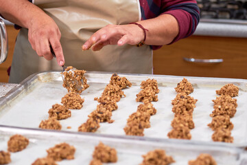Woman places uncooked raw oatmeal cookies on steel tray.