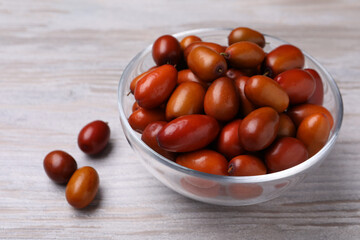 Fresh Ziziphus jujuba fruits with glass bowl on wooden table, closeup