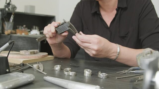 Mid-section shot of unrecognizable female jeweler sitting at workbench and using caliper to measure metal ring
