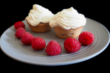 raspberries and two gluten-free muffins with mascarpone cream and cream on a gray round plate on a black background . dessert 