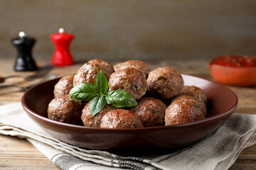 Tasty cooked meatballs with basil served on wooden table
