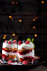 On a wooden background with lights, dessert with cream, cottage cheese, raspberries and blueberries in a glass