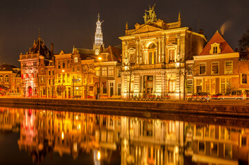 Fototapeta na wymiar Haarlem, The Netherlands, November 19, 2021: historic facades reflect in the water of Spaarne river at night, with in the background the tower of Saint Bavo's church