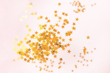 Pink background with confetti and glitter of gold stars. Abstraction of sequins on a light...