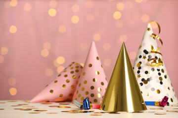 Party hats and festive items on white table against pink background with blurred lights. Space for text