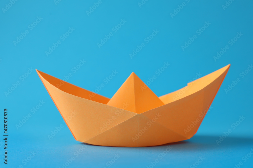 Wall mural Handmade orange paper boat on light blue background. Origami art