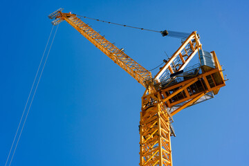A yellow constraction crane against blue sky, London, UK