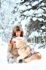 Happy young woman with a husky dog in a snowy forest