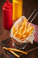French fries in a metal mesh basket on a wooden board. Fast food concept, american food