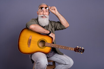 Portrait of attractive cheerful talented popular grey-haired man singer playing guitar isolated over dark violet color background