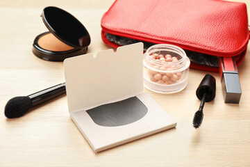 Facial oil blotting tissues and different decorative cosmetics on wooden table. Mattifying wipes
