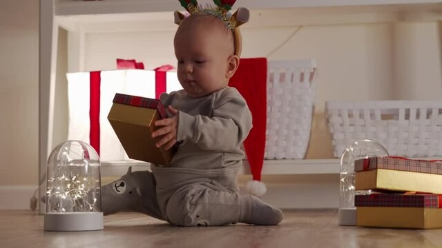 Cute toddler in festive new year reindeer horns holding little gift box, happy kid playing with christmas decorations, child have fun spend New Year time. High quality 4k footage