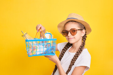 cute teenage girl with a shopping basket on a yellow background, shopping before going to a warm country