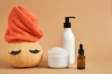 mock up set of cosmetic containers and pumpkin with towel and false eyelashes on beige background