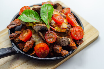 Vegetarian dish of sweet potatoes and mushrooms baked with cheese, served with fresh tomatoes, all served in a cast iron pan