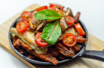 Vegetarian dish of sweet potatoes and mushrooms baked with cheese, served with fresh tomatoes, all served in a cast iron pan