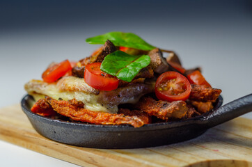 Vegetarian dish of sweet potatoes and mushrooms baked with cheese, served with fresh tomatoes, all served in a cast iron pan