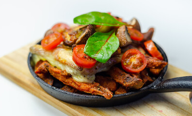 Vegetarian dish of sweet potatoes and mushrooms baked with cheese, served with fresh tomatoes, all served in a cast iron pan