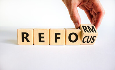 Refocus and reform symbol. Businessman turns a wooden cube and changes the word refocus to reform....