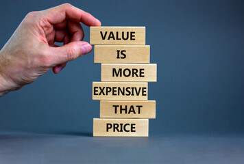 Price or value symbol. Wooden blocks with concept words Value is more expensive that price. Beautiful grey background, copy space. Businessman hand. Business, price or value concept.