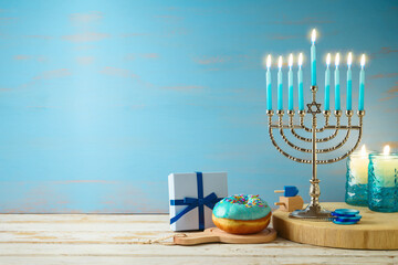 Hanukkah concept with menorah, candles, gift box and traditional donut on wooden table over blue...