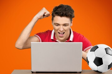 Young fun excited man football fan support team with soccer ball use laptop pc computer