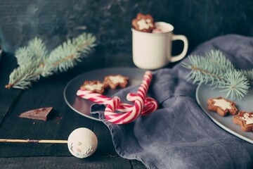 Obraz na płótnie Canvas Christmas, New Year, a cup of coffee with meringues and marshmallows, caramel candies, a plate of cookies on a linen cloth on a dark wooden table, a festive atmosphere, a rustic retro style