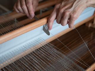 Woman is warping a wooden handloom. Hands holding a heddle hook and threading the table loom....