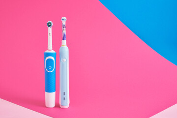 electric blue toothbrushes on bright geometric pink and blue background oral hygiene concept