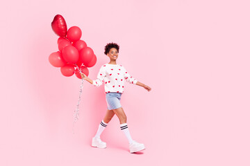 Full size profile side photo of young cheerful woman walk hold many helium balloons isolated over pink color background