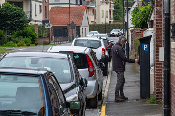A man pays his parking fee at a pay and display machine on a pavement in the city of France