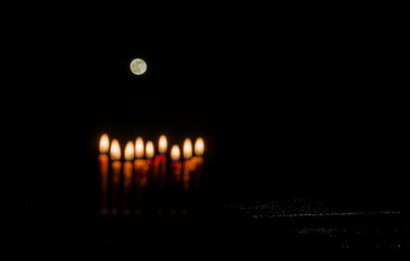 Rising moon in the sky and blurred burning was candles as a symbol of Hanukkah Holiday of Miracle Light