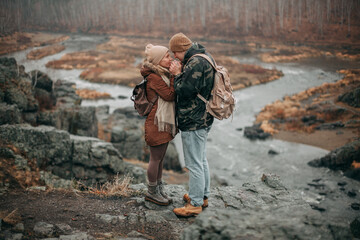A couple in love in autumn stands on a mountain overlooking the river and forest. The man warms the girl's hands and looks at each other