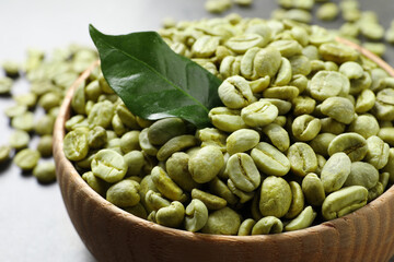 Green coffee beans and leaf in wooden bowl on table, closeup