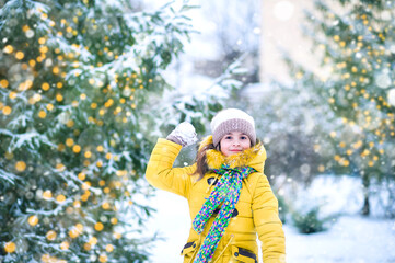 Happy girl in yellow jacket plays with snow. Children games in winter..
