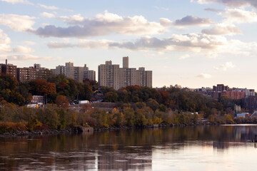 cityscape view of the North Bronx from across the Harlem River at the golden hour, with fall foliage and twilight clouds in the sky - obrazy, fototapety, plakaty