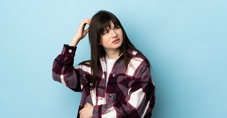 Teenager Ukrainian girl isolated on blue background having doubts while scratching head