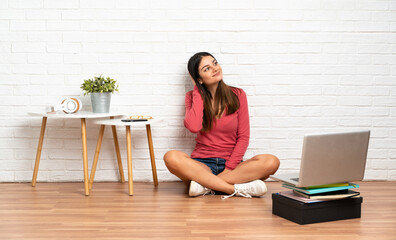 Young woman with a laptop sitting on the floor at indoors thinking an idea