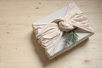 Zero waste gift wrapping. Sustainable design concept. Beige Christmas present with spruce twig on wooden background