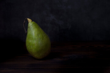 Ripe pear on a wooden table, dark background. Space for text.