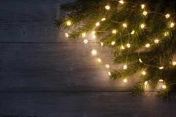 Christmas dark wooden background with fir branches, light garland and space for text, postcard for...