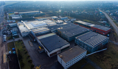 Naklejka premium Numerous solar panels mounted on the industrial building. Applying spacious roof area for producing clean energy. View of the rural area at the background.