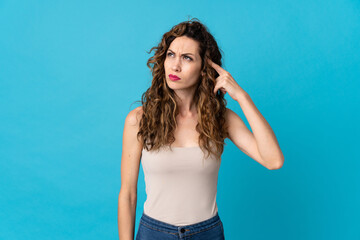 Young caucasian woman isolated on blue background making the gesture of madness putting finger on...