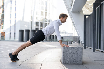 Sportive man training outdoors, doing push ups from box