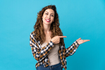 Young caucasian woman isolated on blue background holding copyspace imaginary on the palm to insert an ad