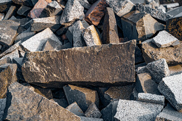 Huge boulders of broken granite, grey and brown in color. Cobblestones in a pile under the shining sun close up.